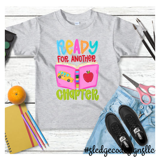 Ready for Another Chapter Teacher Shirt featuring an open book, school bus, and apple on a custom unisex T-shirt by Sledge Co Designs.