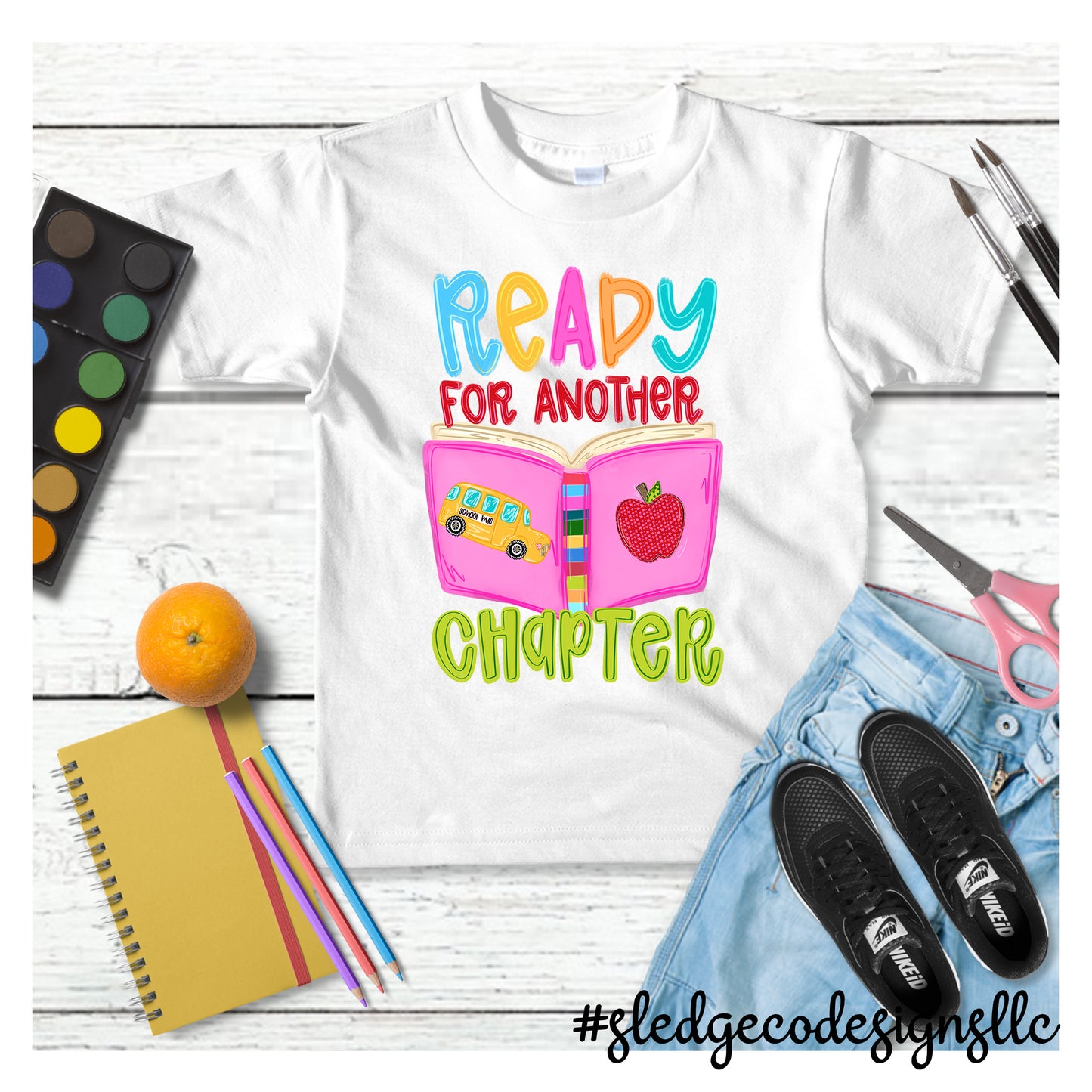 Ready for Another Chapter Teacher Shirt featuring an open book, school bus, and apple on a custom unisex T-shirt by Sledge Co Designs.